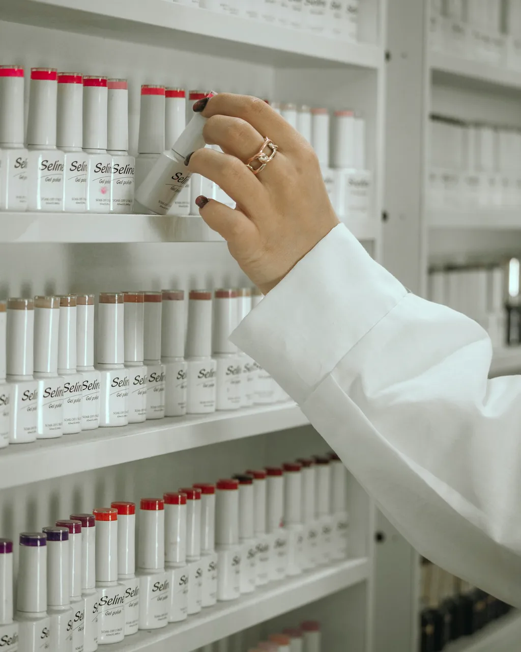 Una farmacéutica con bata blanca coge un producto de la estantería de dermocosmética
