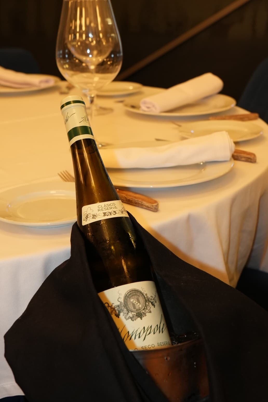 Botella de vino blanco en cubitera junto a la mesa