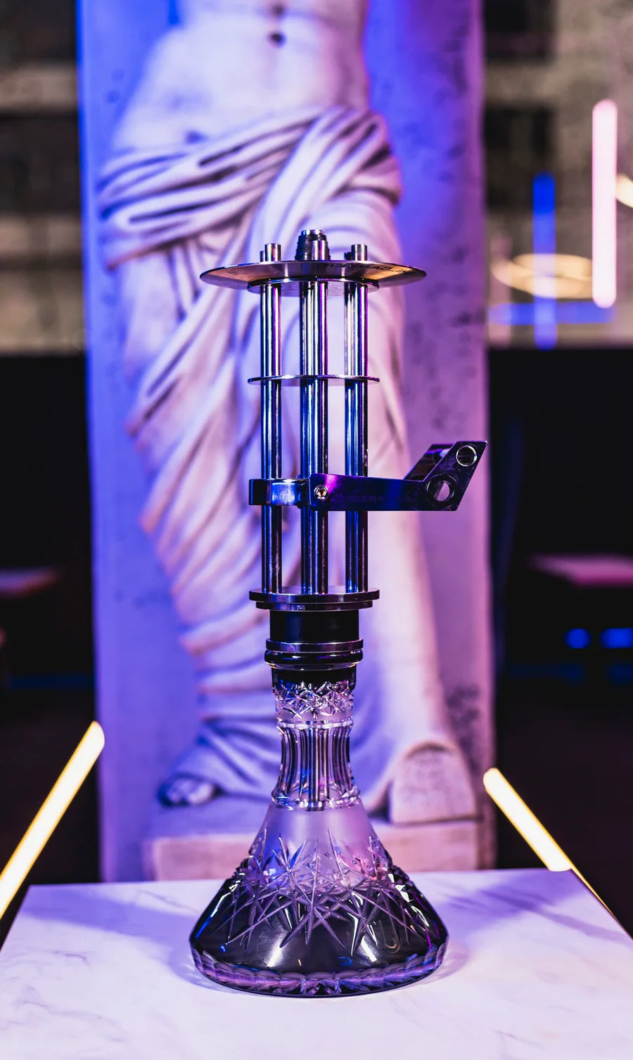 Cachimba Shi Carver Minigun, de acero con varillas, delante de una estatua clásica iluminada de azul