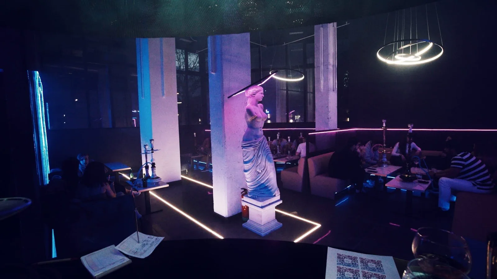 El salón de Psyko de noche: columnas blancas, una estatua clásica con luz rosa, neones en el suelo y sofás