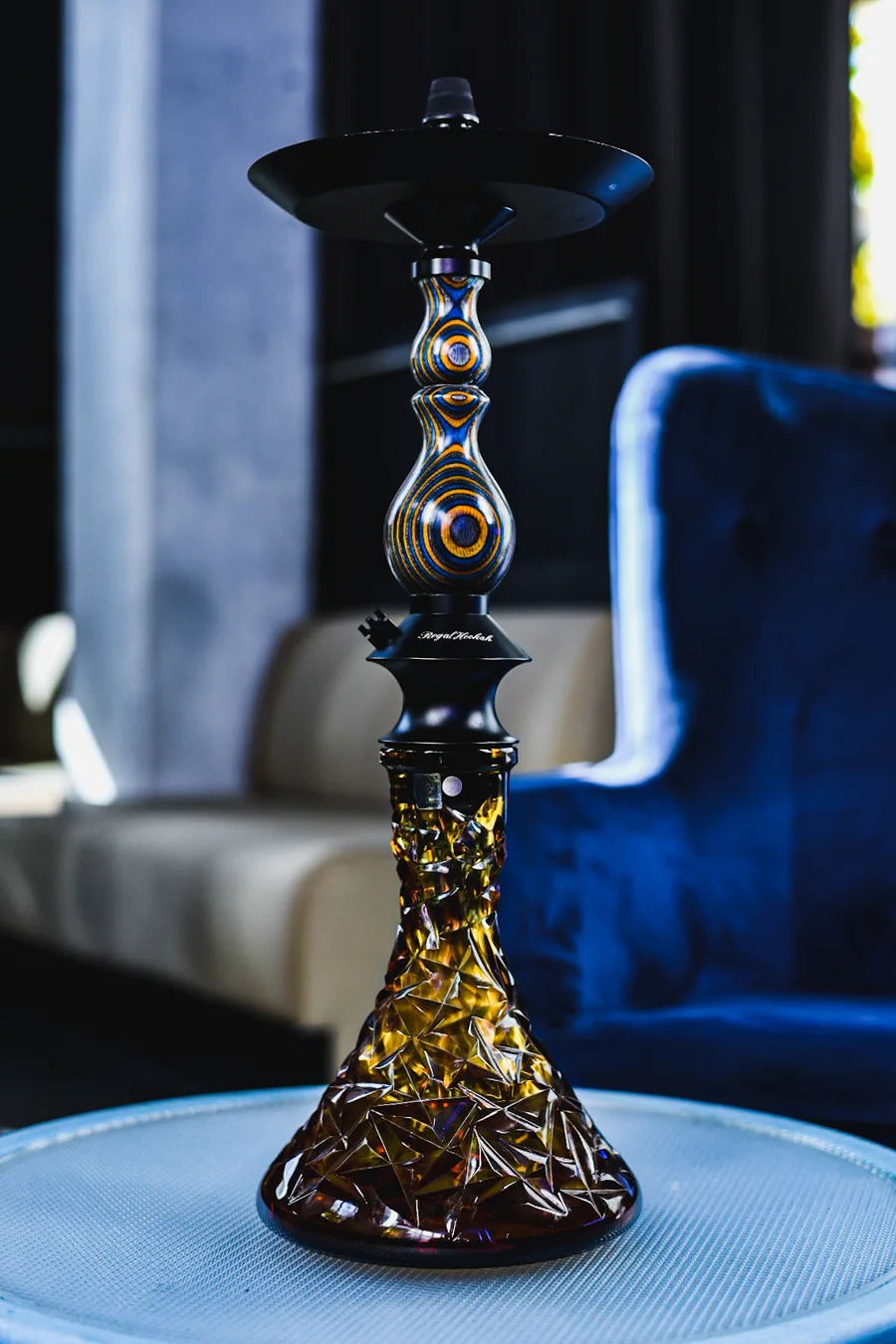 Cachimba negra y dorada sobre una mesa, junto a los sofás de terciopelo azul