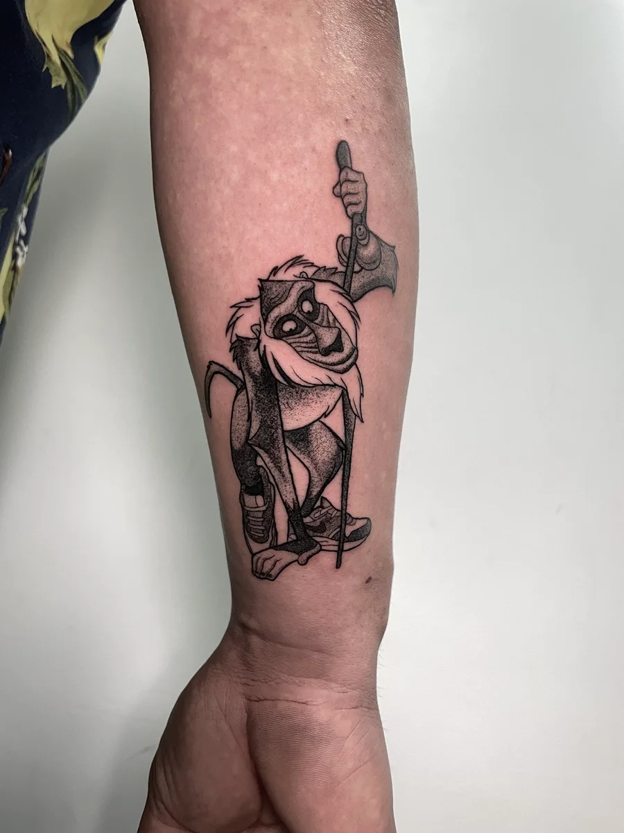 Rafiki de El rey león en estilo cartoon, tatuado en el antebrazo